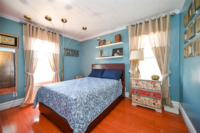 bedroom with baseboards, ornamental molding, and wood finished floors