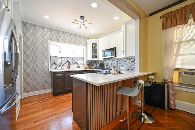 kitchen featuring a breakfast bar, light countertops, stainless steel appliances, a peninsula, and glass insert cabinets
