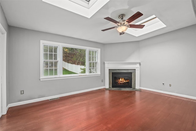 unfurnished living room featuring a skylight, wood finished floors, visible vents, ceiling fan, and a fireplace with flush hearth