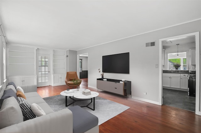 living room with wood finished floors, built in shelves, baseboards, and crown molding