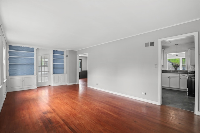 unfurnished living room featuring hardwood / wood-style flooring, built in features, baseboards, a sink, and crown molding