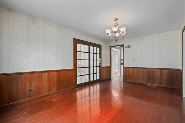 spare room featuring a chandelier, wainscoting, hardwood / wood-style floors, and wood walls