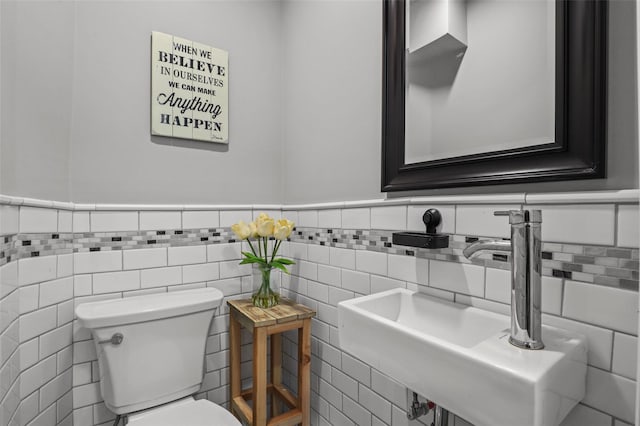 half bath with a sink, tile walls, toilet, and a wainscoted wall