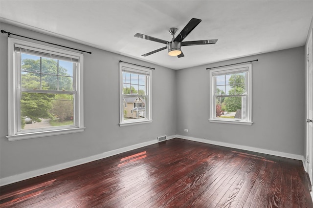 spare room with a wealth of natural light, visible vents, baseboards, and dark wood-style floors