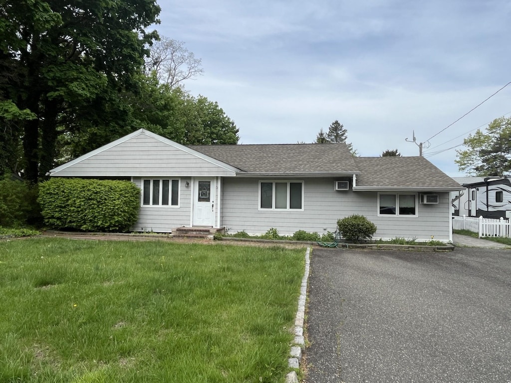 ranch-style house with a shingled roof, fence, and a front yard