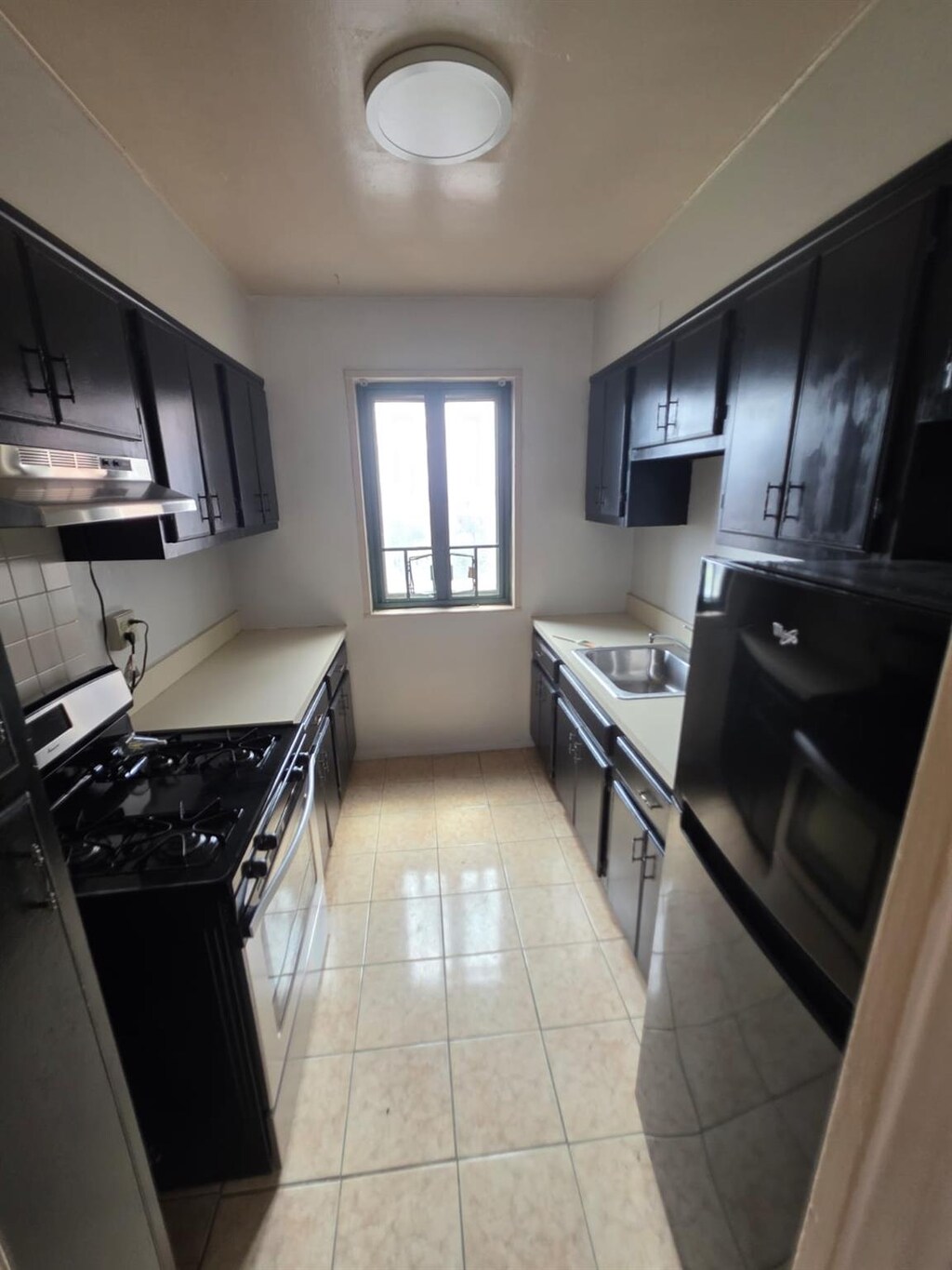 kitchen with a sink, freestanding refrigerator, stainless steel range with gas cooktop, dark cabinets, and under cabinet range hood