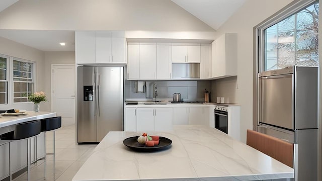 kitchen with freestanding refrigerator, lofted ceiling, oven, stainless steel fridge with ice dispenser, and a sink