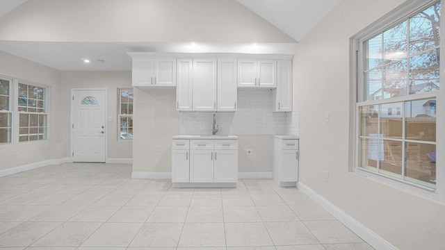 kitchen featuring tasteful backsplash, vaulted ceiling, a sink, white cabinets, and light tile patterned flooring