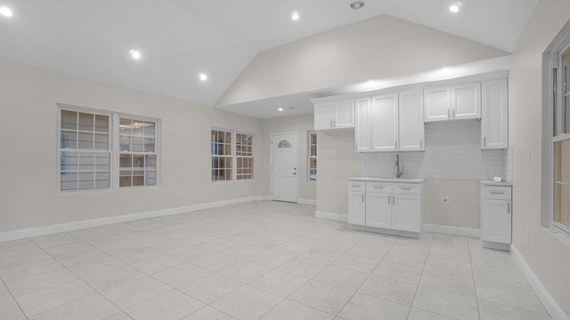 kitchen featuring light tile patterned flooring, a sink, white cabinetry, lofted ceiling, and backsplash
