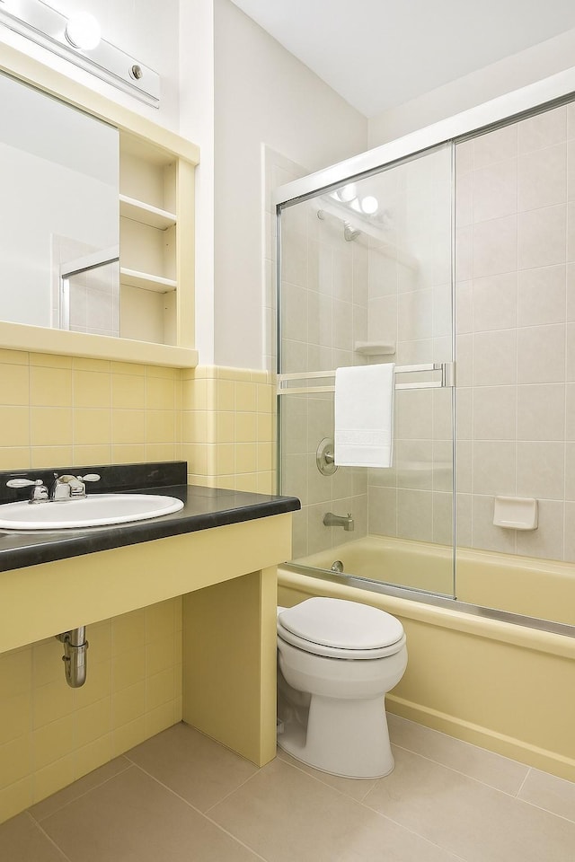 bathroom with a sink, tile patterned flooring, toilet, and bath / shower combo with glass door