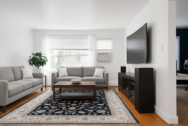 living room featuring baseboards, cooling unit, a healthy amount of sunlight, and light wood-style flooring