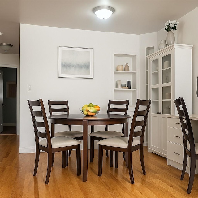 dining room featuring light wood-type flooring, built in features, and baseboards