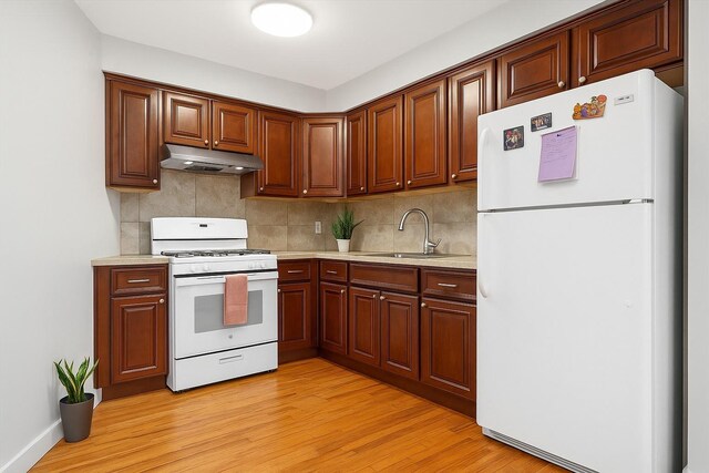 kitchen featuring a sink, white appliances, light wood-type flooring, under cabinet range hood, and light countertops