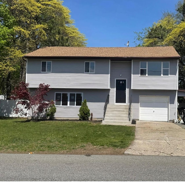 bi-level home featuring an attached garage, concrete driveway, a front yard, and entry steps