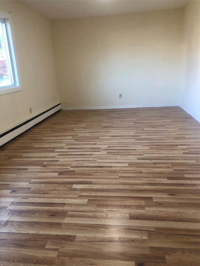unfurnished room featuring baseboards, a baseboard heating unit, and wood finished floors