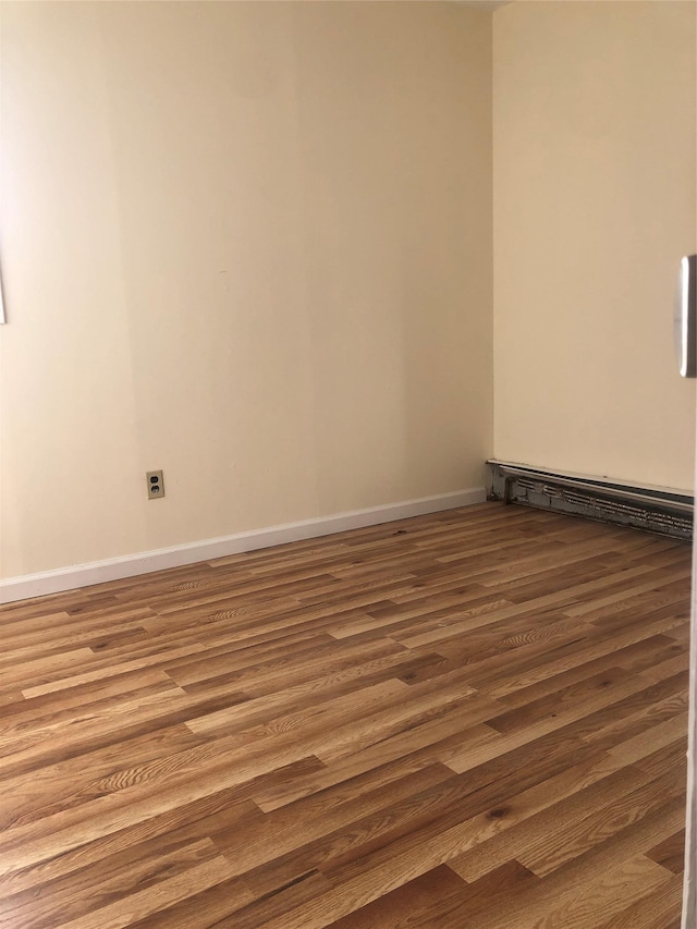 empty room with baseboards, a baseboard heating unit, and wood finished floors