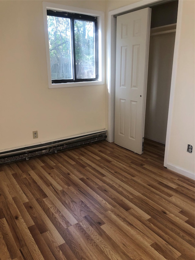 unfurnished bedroom with wood finished floors, a baseboard heating unit, and a closet