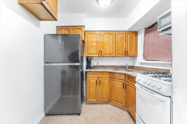 3135 Gunther Ave, Bronx, NY 10469 - kitchen featuring brown cabinetry, a sink, light countertops, white gas range oven, and freestanding refrigerator