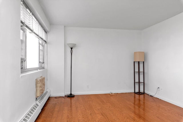 spare room with baseboards, a baseboard radiator, and wood finished floors