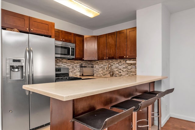 kitchen featuring tasteful backsplash, light countertops, a sink, a peninsula, and stainless steel appliances