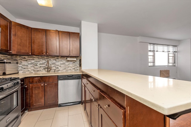 kitchen with a peninsula, light countertops, a sink, appliances with stainless steel finishes, and backsplash