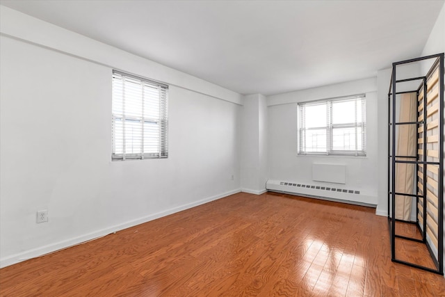 unfurnished room featuring baseboards, wood finished floors, and a baseboard radiator