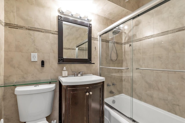 bathroom with vanity, toilet, shower / bath combination with glass door, and tile walls