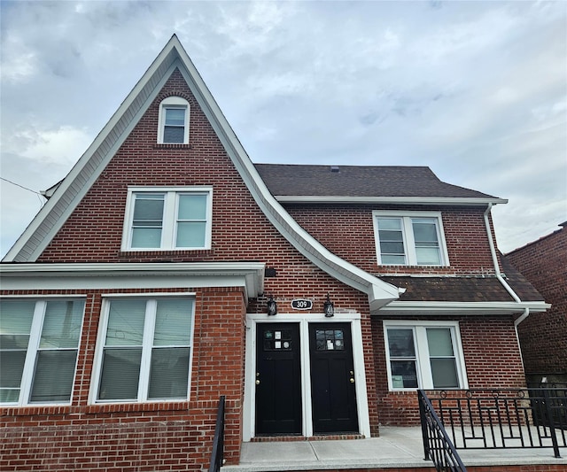 view of front facade with roof with shingles and brick siding