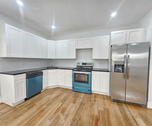 kitchen with appliances with stainless steel finishes, dark countertops, white cabinetry, a sink, and light wood-style flooring
