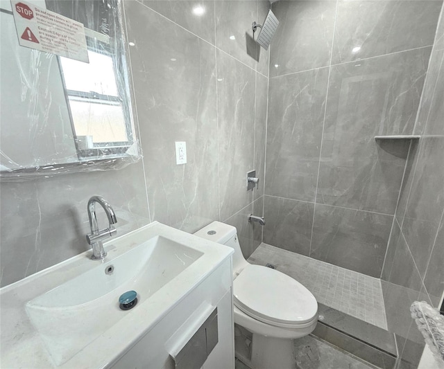 bathroom with tile walls, vanity, toilet, and tiled shower