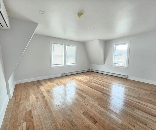 bonus room with light wood-style floors, baseboards, a baseboard heating unit, and a wall mounted air conditioner