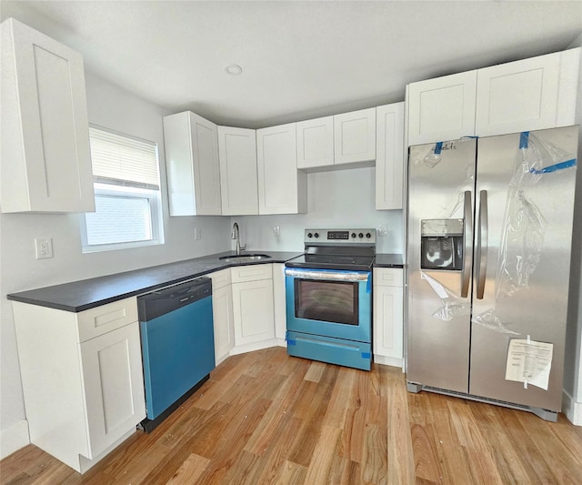 kitchen with dark countertops, appliances with stainless steel finishes, white cabinetry, a sink, and light wood-style flooring