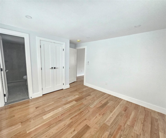 unfurnished bedroom featuring baseboards, a closet, light wood-type flooring, and connected bathroom