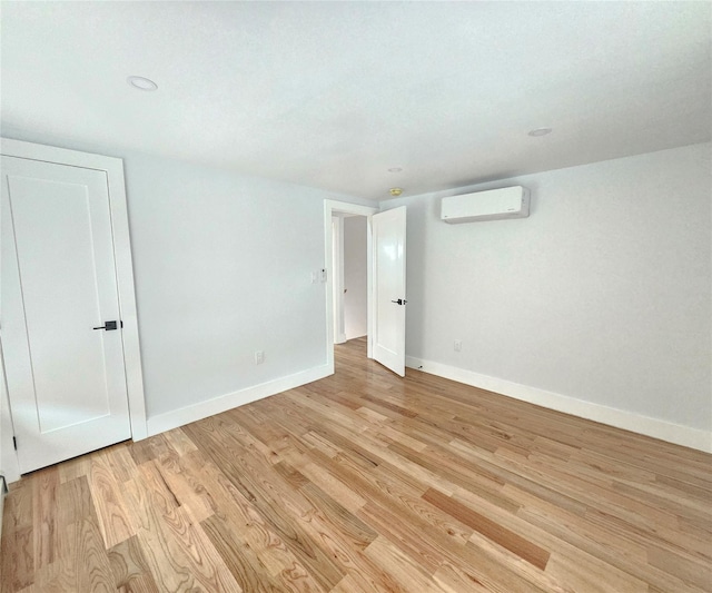 empty room featuring baseboards, an AC wall unit, and light wood-type flooring
