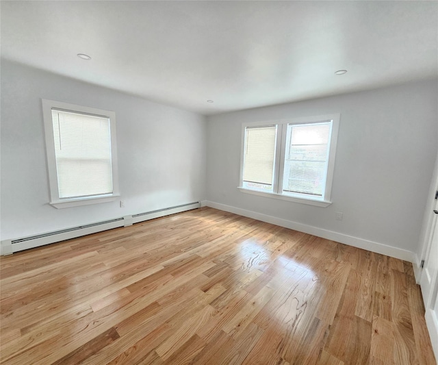 empty room featuring baseboards, a baseboard heating unit, and light wood finished floors