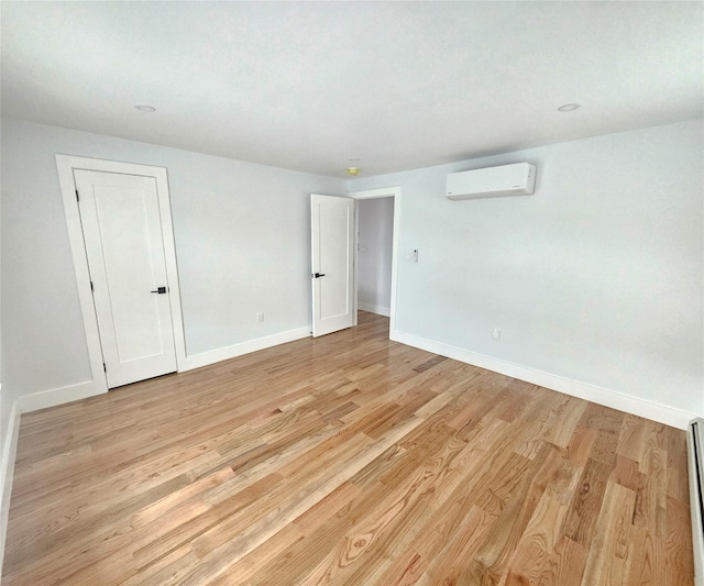 unfurnished room with baseboards, a baseboard radiator, light wood-style flooring, and a wall unit AC