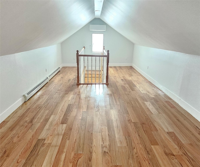 additional living space featuring a wall mounted AC, vaulted ceiling, baseboards, a baseboard radiator, and light wood finished floors