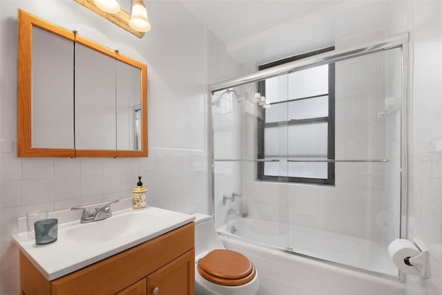 bathroom featuring tile walls, enclosed tub / shower combo, vanity, and toilet