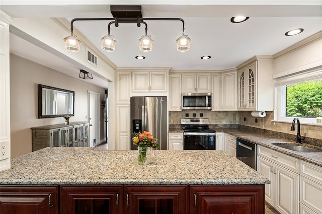 kitchen featuring light stone counters, a sink, a center island, stainless steel appliances, and cream cabinetry