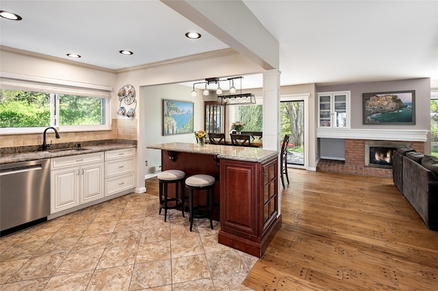 kitchen with a breakfast bar area, backsplash, light stone countertops, dishwasher, and a sink