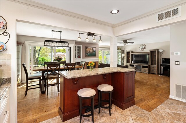 kitchen featuring a breakfast bar, light stone countertops, open floor plan, and visible vents