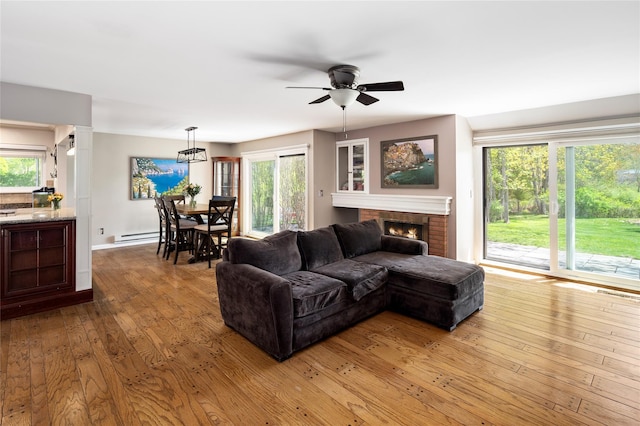 living room with a brick fireplace, hardwood / wood-style floors, baseboards, ceiling fan, and baseboard heating