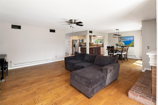 living room featuring light wood-style floors, ceiling fan, a baseboard heating unit, and visible vents