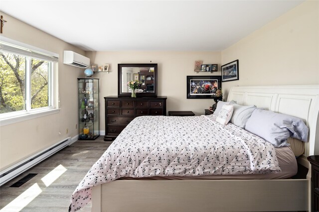 bedroom with baseboards, baseboard heating, an AC wall unit, and wood finished floors