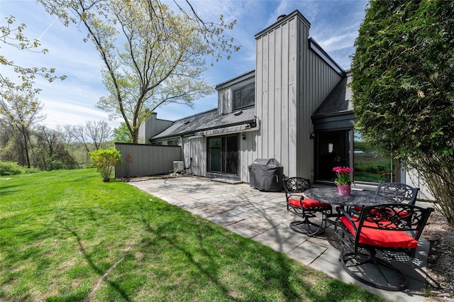 rear view of property with a lawn, a patio area, roof with shingles, and a chimney