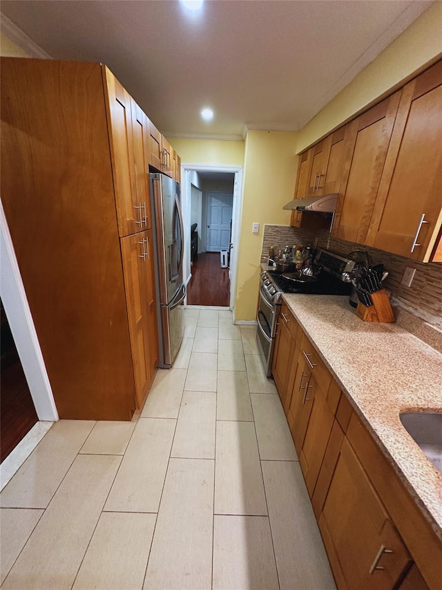 kitchen featuring brown cabinets, under cabinet range hood, baseboards, and appliances with stainless steel finishes