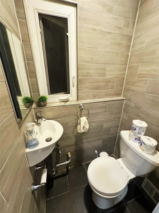 bathroom featuring a sink, tile patterned floors, toilet, and tile walls