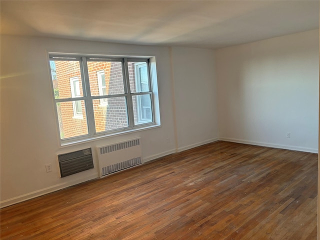 unfurnished room featuring baseboards, a wealth of natural light, radiator heating unit, and hardwood / wood-style flooring