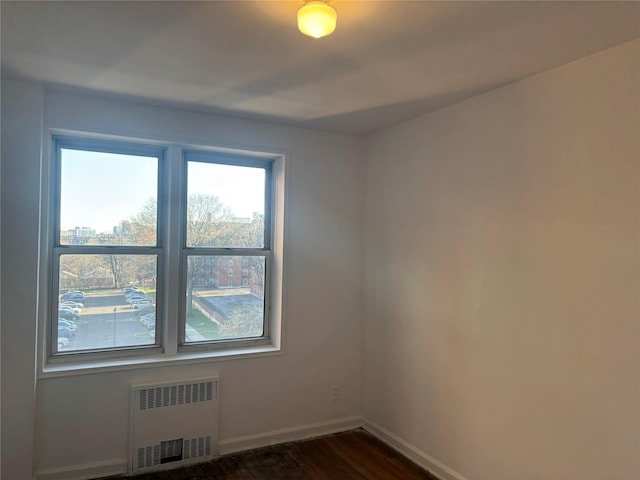 unfurnished room with radiator heating unit, baseboards, and dark wood-style floors