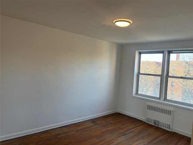 empty room featuring dark wood-style flooring, baseboards, and radiator
